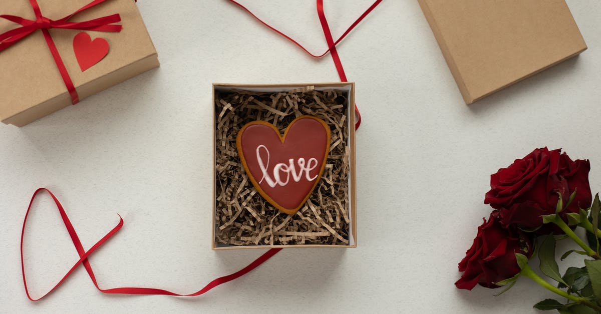 Filling vs Frosting - Top view of heart shaped cookie with Love word in box with decorative paper filling [laced on gray background near gift boxes with red ribbons and bouquet of roses