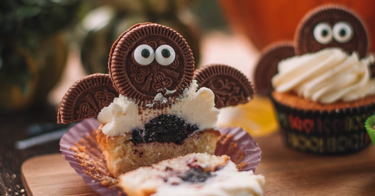 Filling vs Frosting - Tasty cut cupcake with sweet filling and frosting decorated with cookie placed on wooden cutting board in room on blurred background