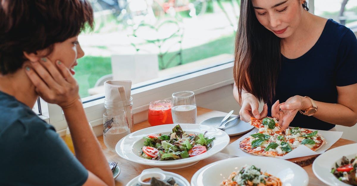 First time dashi doesn't taste much - Content Asian woman taking slice of pizza while sitting at table near friend with delicious salad and pasta in restaurant
