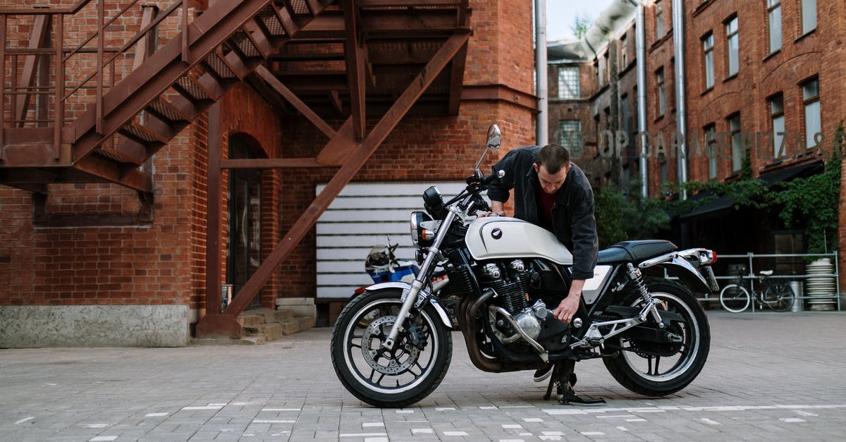 Fixing a Brownie Brick - Man Fixing Motorcycle Parked Beside Brick Building