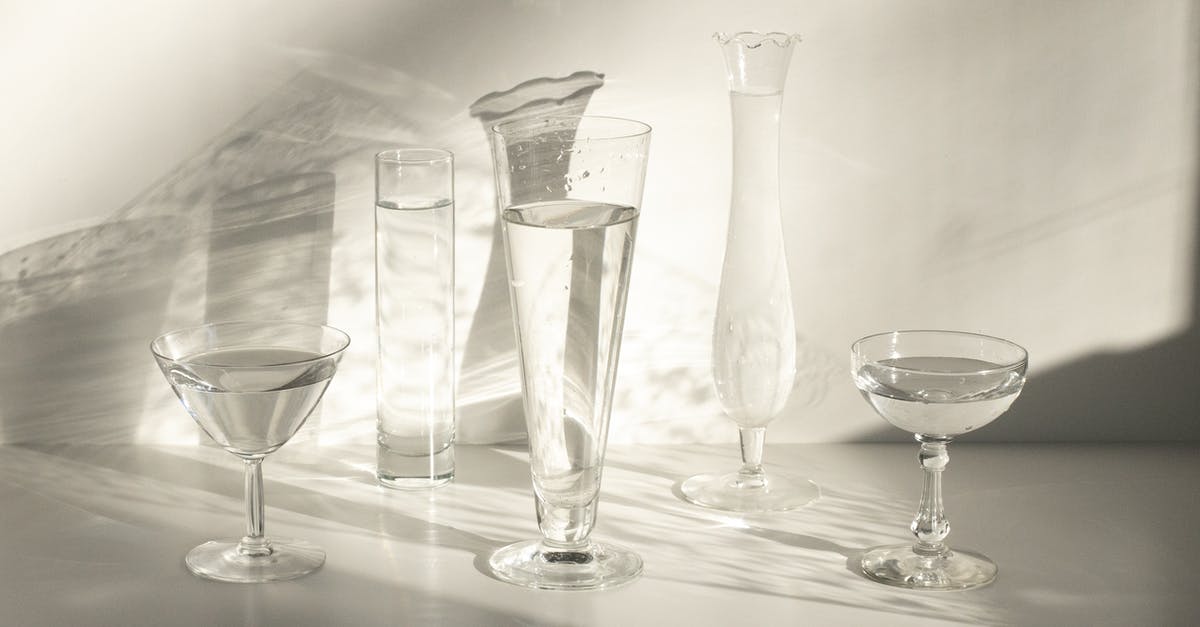Flambe, alcohol percentage and water residue - From above set of classic crystal glasses of various shapes with water served on white table in sunlight