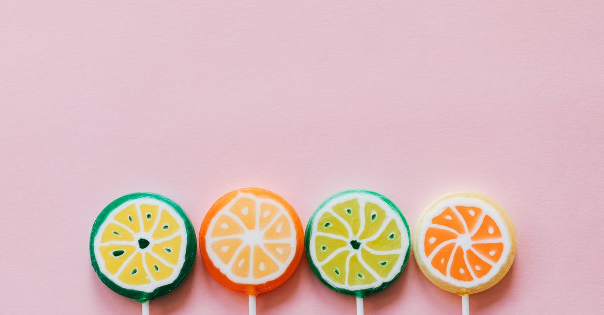 Flavor difference between marzipan and persipan - Top view of round multicolored candies with citrus fruit flavor on thin plastic sticks on pale pink surface