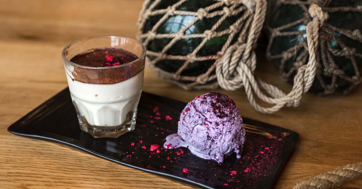 Food dye to simulate stained glass - From above of glass of cream dessert with chocolate top served with blueberry ice cream scoop dusted with pink dye placed on ceramic plate on wooden table near black glass balls in grid of rope