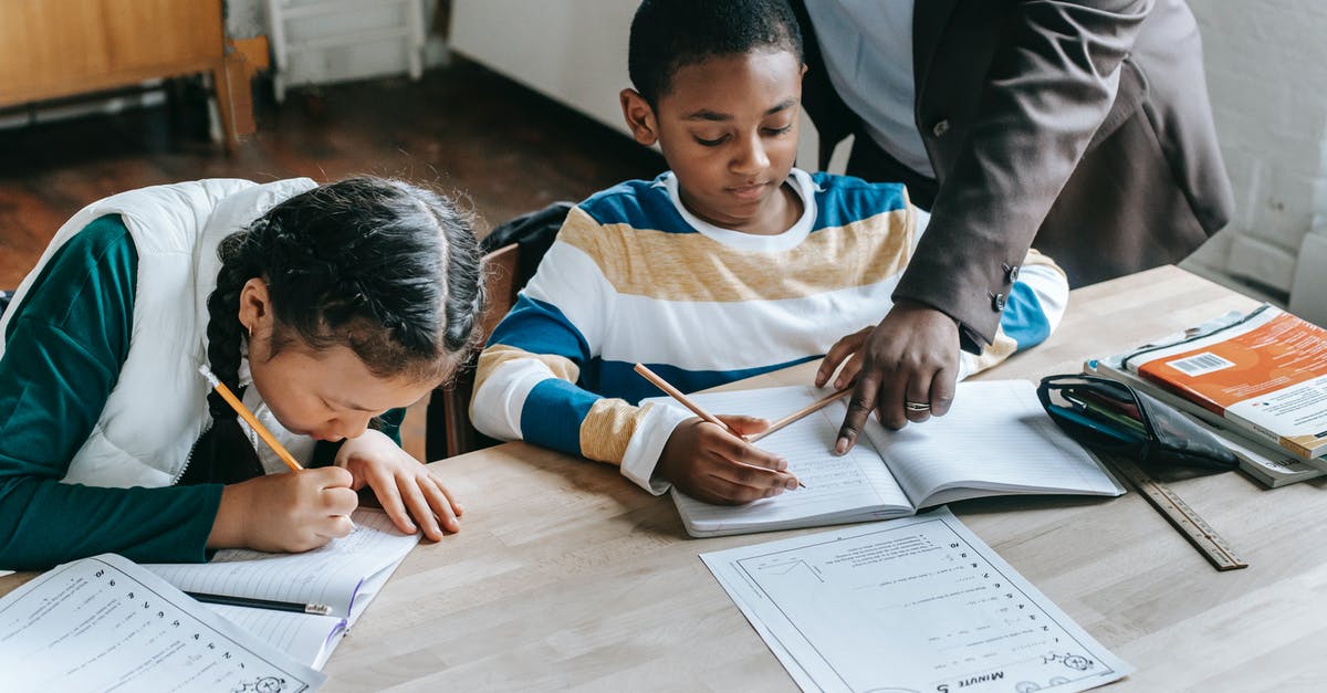 Foolproof Pectin test - High angle of crop unrecognizable black female teacher explaining task to focused little schoolboy sitting at desk near attentive Asian classmate writing in notebook