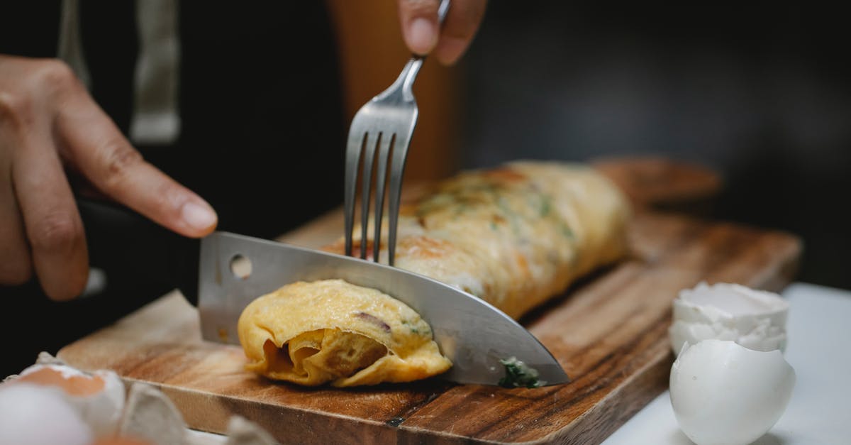 Forgotten Fried Eggs Recipe - Crop anonymous cook with knife and fork cutting yummy hot egg roll on wooden board