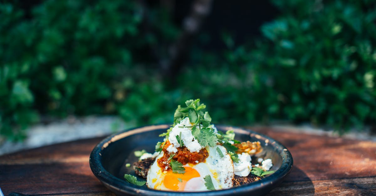 Forgotten Fried Eggs Recipe - Appetizing fried eggs covered with verdant parsley in plate on timber round shaped table near trees