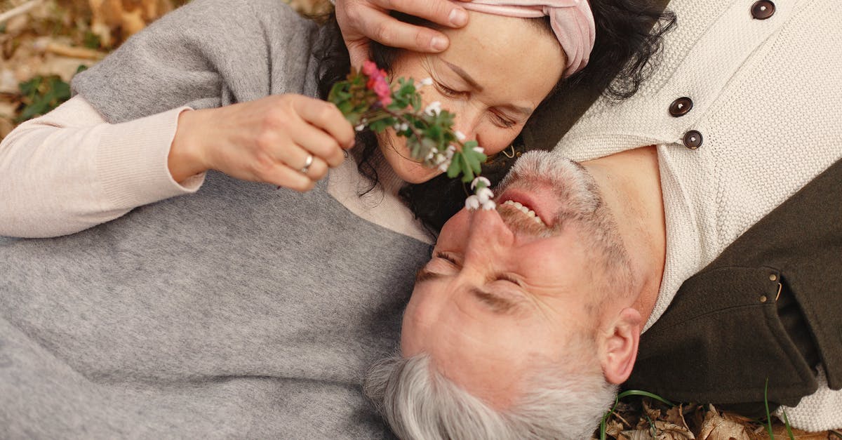 Fresh ground chorizo - From above of cheerful senior wife wearing wide scarf and headband with flower bouquet in hand and happy elderly gray haired husband in warm clothes lying on ground with fallen leaves in park with closed eyes