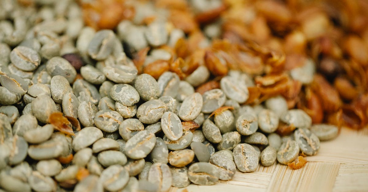 Fresh half and half curdles in hot coffee - Pile of unroasted coffee bean halves with husk on bamboo surface during drying process on blurred background