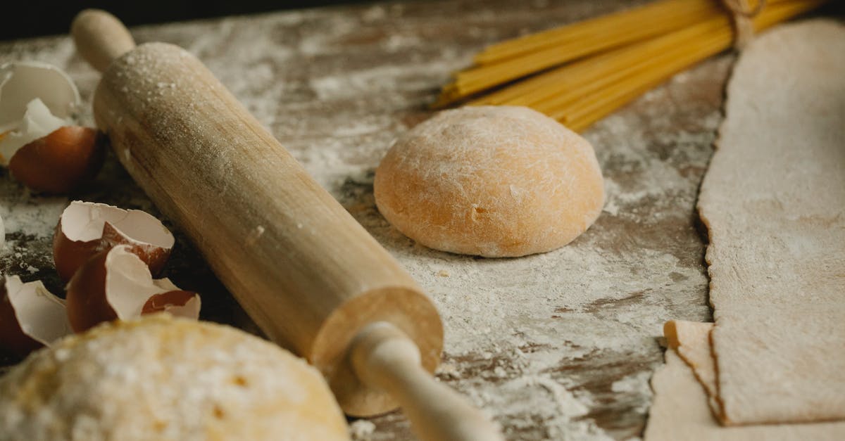 Fresh pasta work surface - Uncooked balls of dough near rolling pin placed on wooden table sprinkled with flour with eggshell and raw spaghetti in kitchen