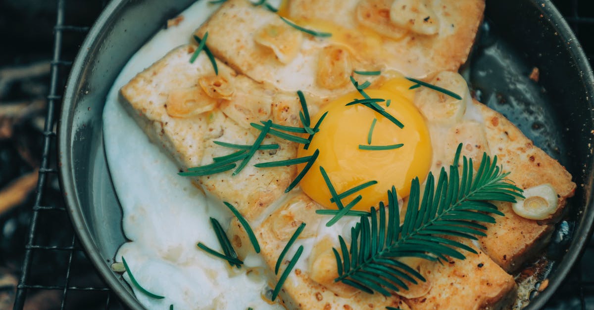 Fried garlic turning black - From above appetizing grilled toasts under egg with rosemary cooked on frying pan on barbecue grid