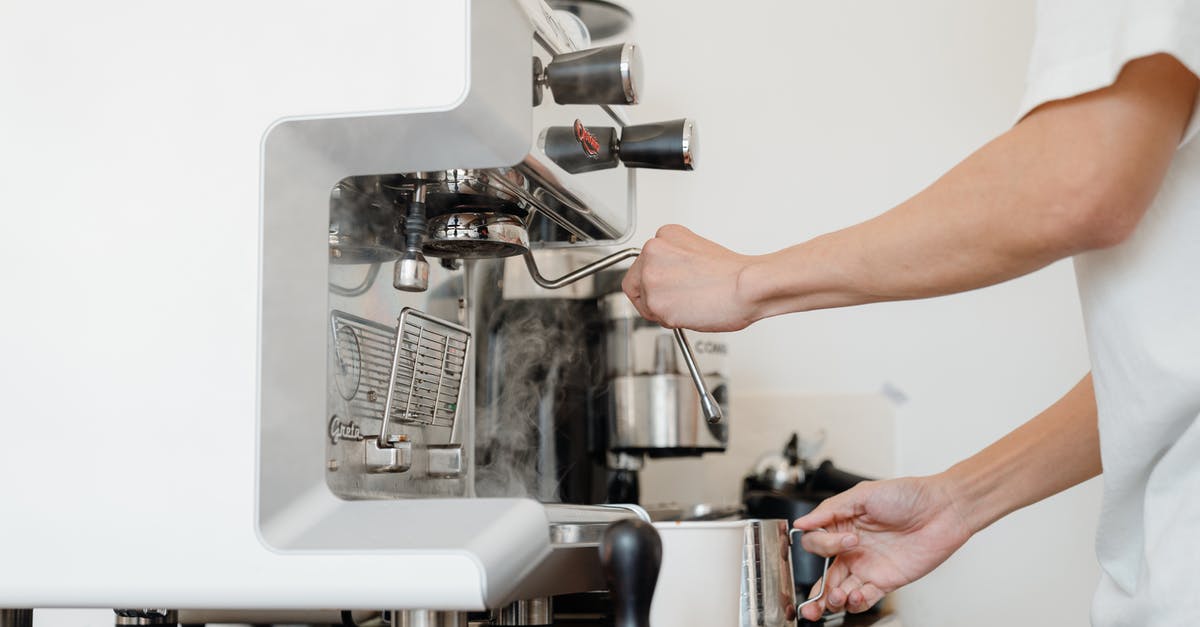 Frothing Milk By Hand - Side view crop anonymous barista in white shirt preparing to steam milk in frothing pitcher using professional coffee machine steam wand