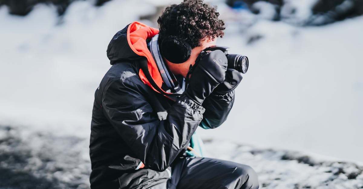 frozen chips always take longer - Side view of male photographer with curly hair in gloves squatting near snowy ground while taking pictures on camera of frozen scenery