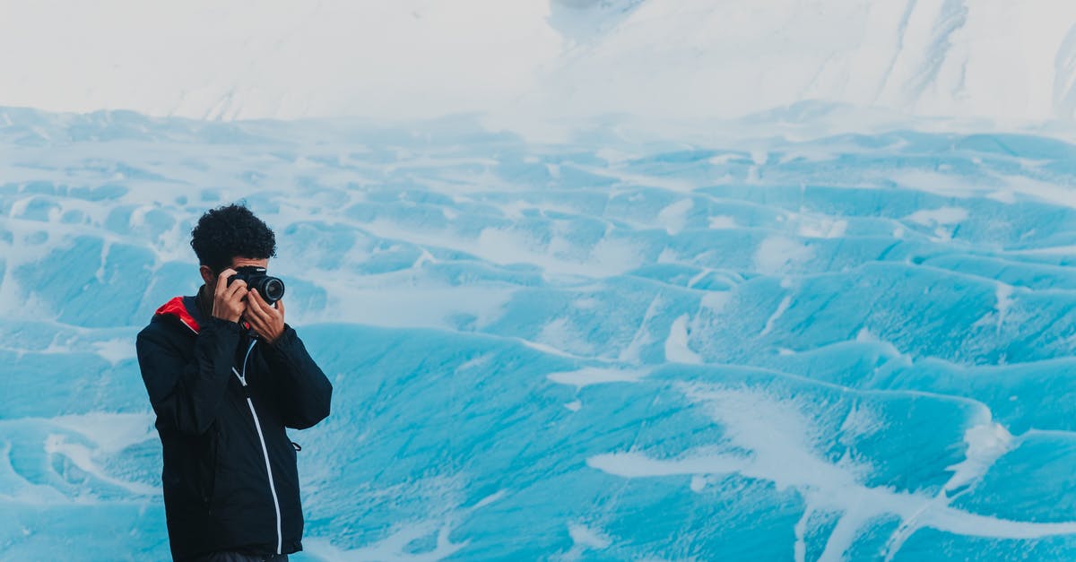 frozen chips always take longer - From above of male photographer standing near snowy pit and taking pictures of frozen surface while spending day in nature