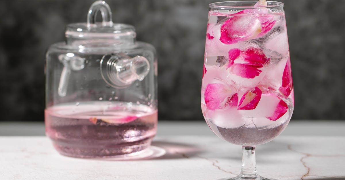 Frozen fresh figs to make jellies - Crystal glass full of fresh beverage with pink rose petals and ice cubes place on table near jar with drink