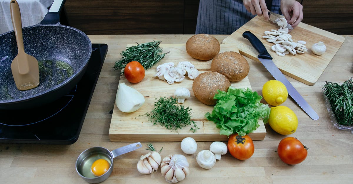 Fry onions and garlic before adding to the sauce? - Crop anonymous female chef wearing apron cutting fresh mushrooms while standing at table with scattered ripe vegetables including onions tomatoes and potatoes in modern kitchen