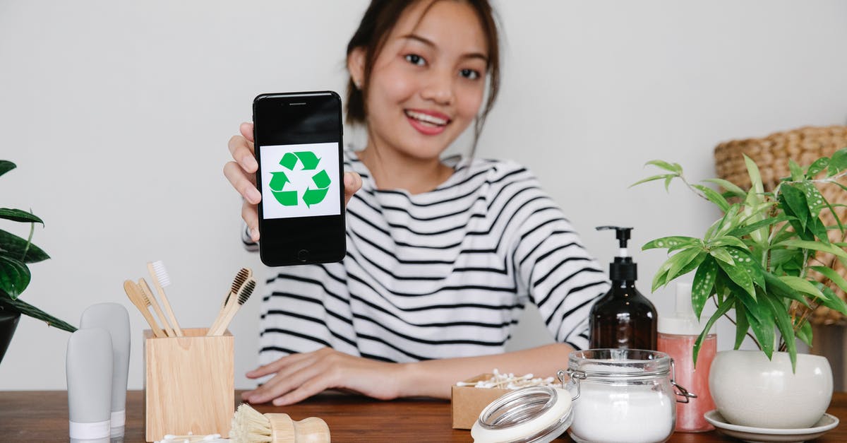 Funnel-like device for putting non-liquids into a whipped cream dispenser? - Smiling Asian woman demonstrating recycling symbol on smartphone while sitting at table with eco friendly cosmetic products and looking at camera