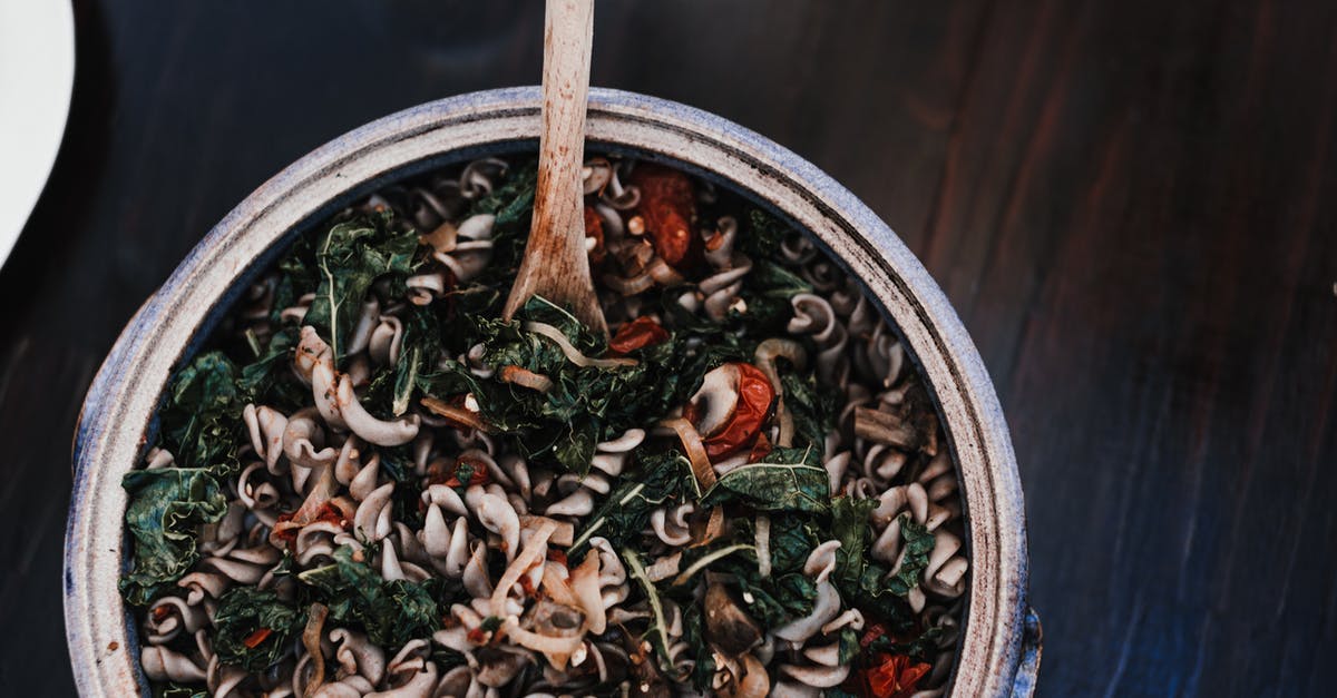 Furman's Italian Style Tomatoes - Top view of appetizing fusilli mixed with spinach leaves and sun dried tomatoes in bowl with wooden spatula