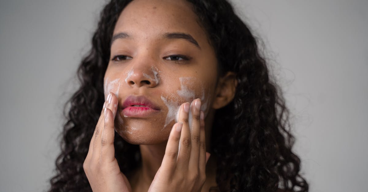 Gari as subtitutes for tapioca - African American female with long dark curly hair washing cheeks with facial foam on gray background