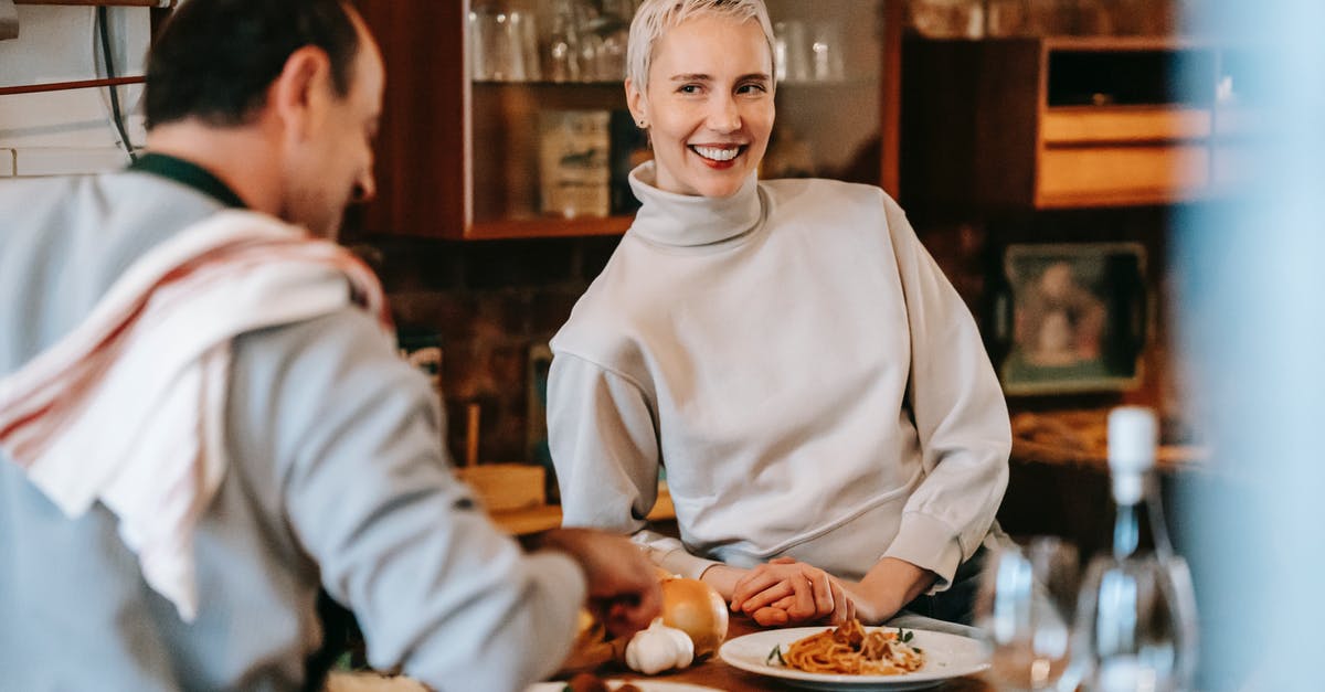 Garlic wine jelly - Smiling adult couple in casual clothes having dinner while male cooking pasta on plates at counter near glasses and wine bottle near various products and ingredients in light kitchen