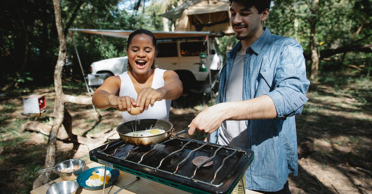 Gas burner is "clicking" - how can I stop this? - High angle of positive multiracial couple frying eggs on skillet using metal gas stove on wooden table near car and tent in forest