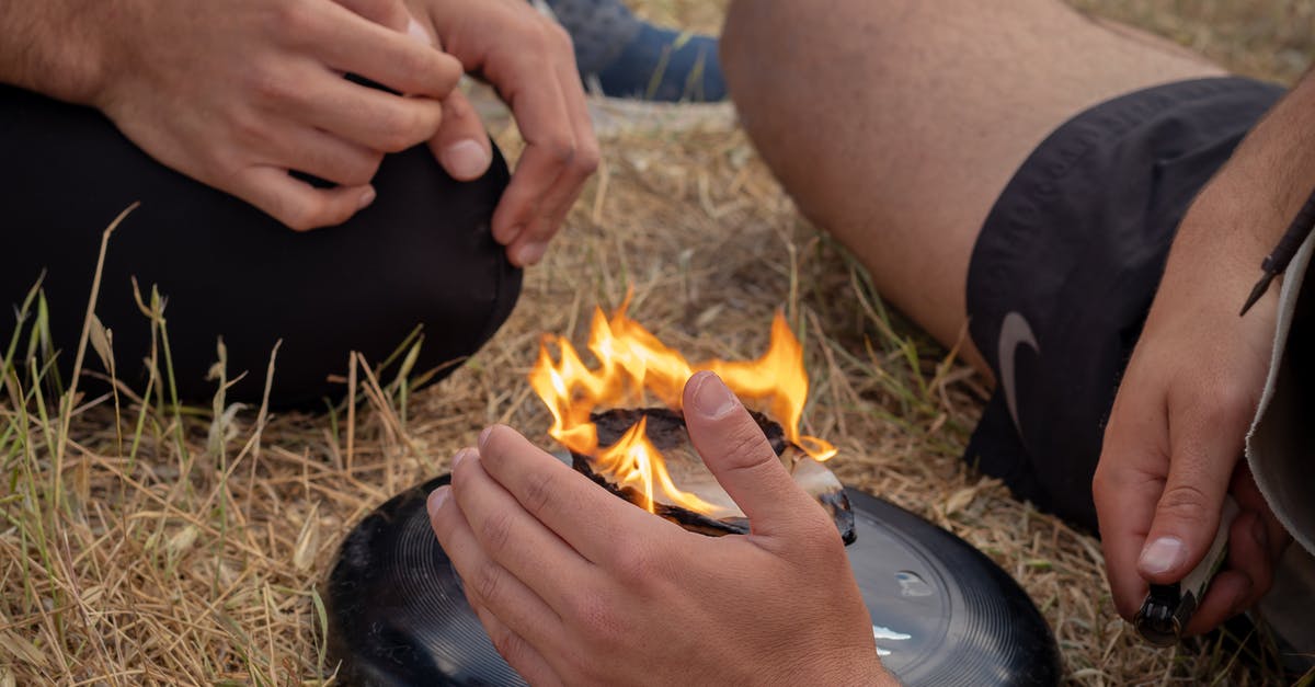 Gas leak (and flames) around burner intake - From above of crop anonymous men friends sitting near burning camping stove in nature in daytime