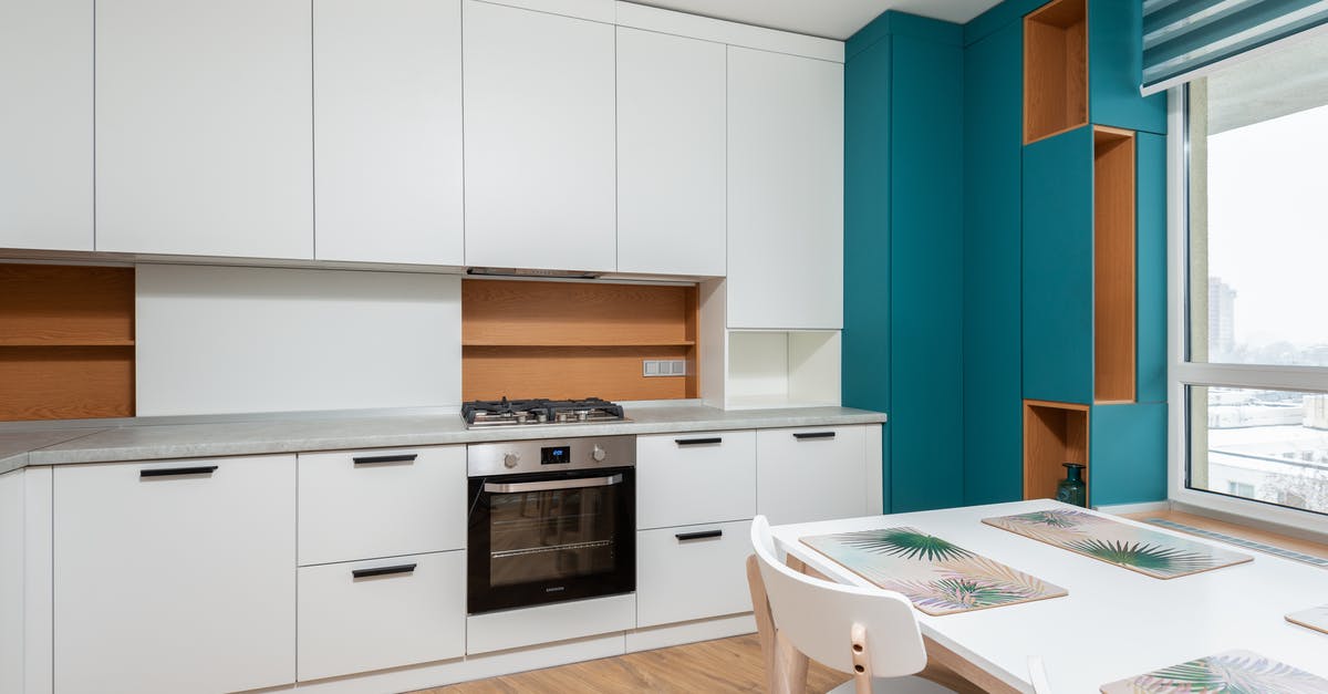 Gas or electric oven with gas stove - Modern cabinet with gas stove and oven against table with placemats under light bulbs in apartment