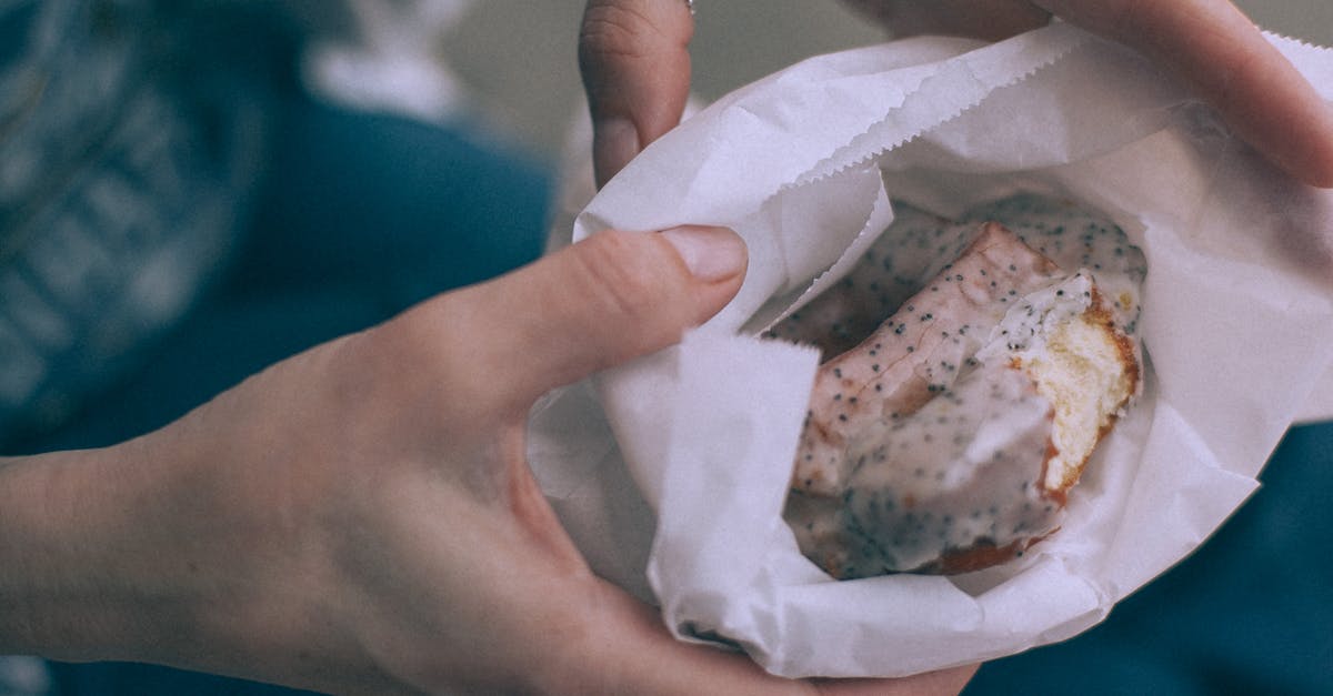 Getting poppy seeds to stick to bagel - From above of crop unrecognizable person showing tasty sweet donut with glaze in organic bag on street