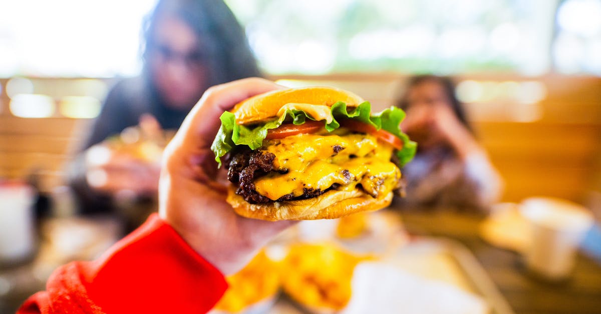 Getting the lighter fluid taste out of burgers, after the fact - Crop anonymous person sitting at table and reaching out hand and demonstrating tasty cheeseburger in cafe in daylight