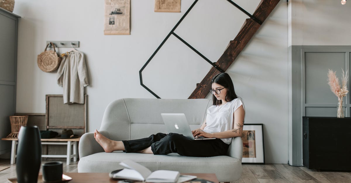 Giant parsnip from Korean shop - Positive female with tattooed arms wearing casual clothes and eyeglasses reading netbook while sitting barefoot on comfortable sofa behind table with books and magazines in modern apartment with minimalist interior in eco style during free time