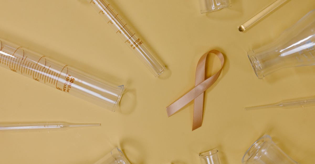 Glass cooktop safety - Top view of pink ribbon representing cancer placed on yellow background among glass test tubes and flasks in light studio