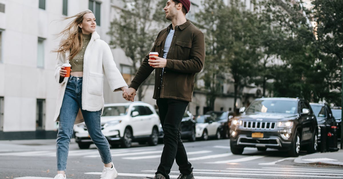 gluten free hot cross buns - Young couple wearing warm jackets and with paper cups of hot drinks crossing road holding hands and looking at each other