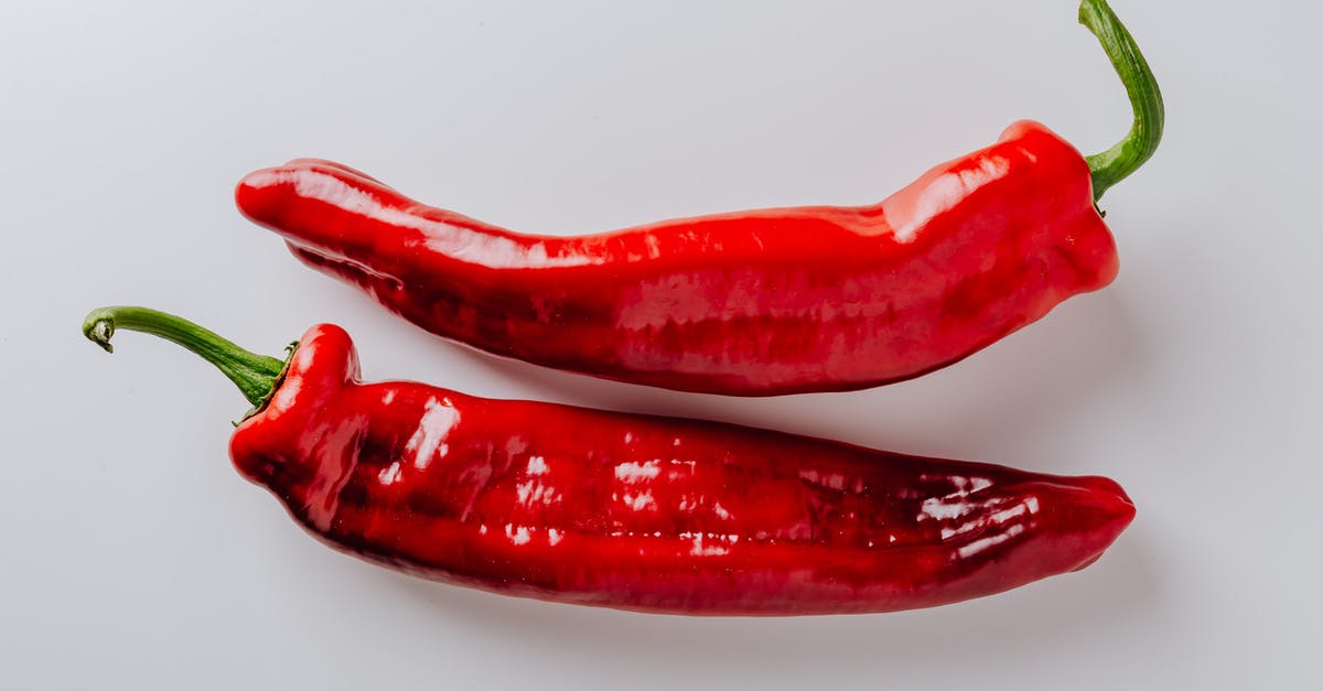 Grilling veggies & meat on same surface for vegetarian guests - From above of pair of hot chili peppers with green sprouts and smooth surface put on white table