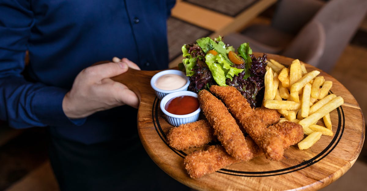 Half cooked fried fish - Hand Holding Round Wooden Chopping Board with Food