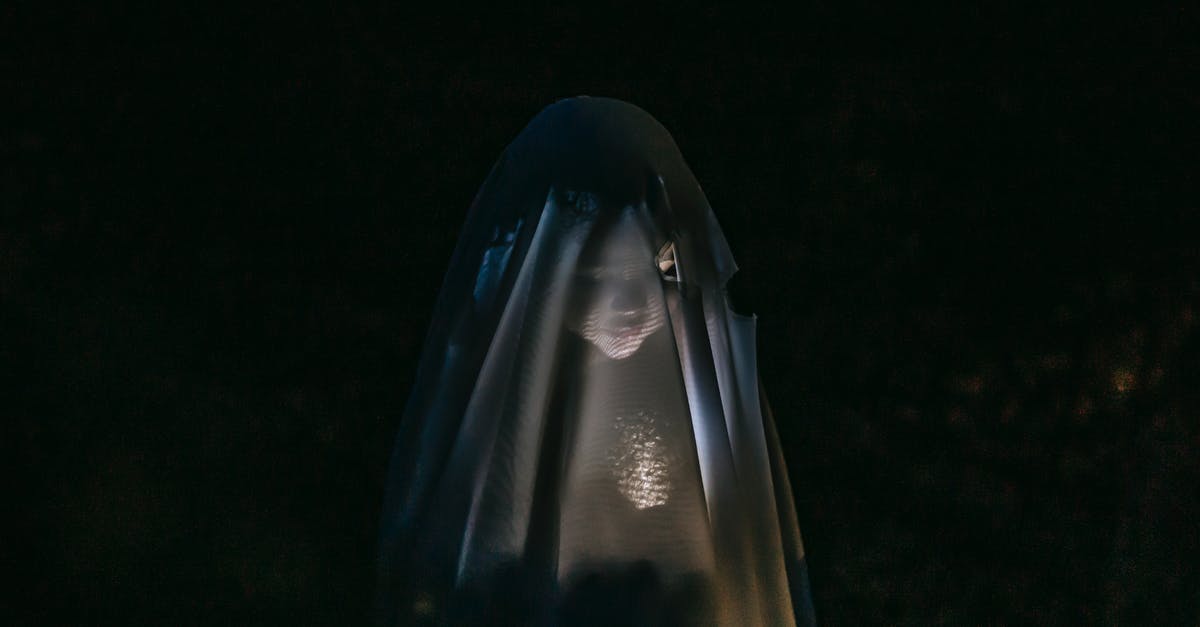 Halloween Special: Glow in the dark food - Mysterious little girl standing in darkness covered with white blanket as ghost and shining flashlight on face