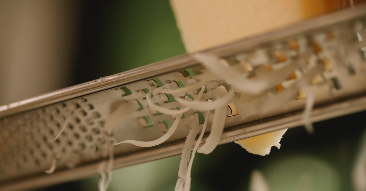 Haloumi cheese is very hard - Closeup of tasty hard cheese grating on narrow stainless grater against blurred kitchen background