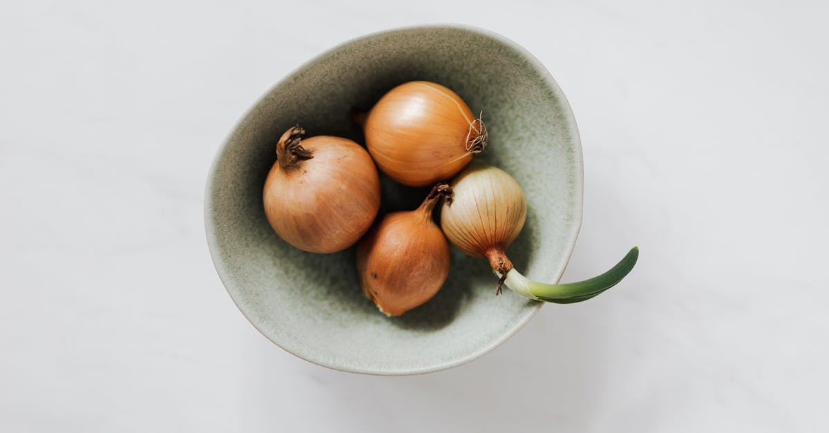 Hamilton Beach 5 qt Slow Cooker Bad taste and smell - Top view of light green bowl with unpeeled raw organic yellow onion bulbs and one regrowing onion placed on white marble tabletop