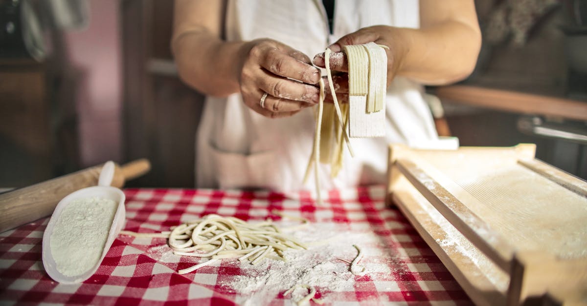 Hand made pasta with wholemeal flour - Unrecognizable cook in uniform standing at table doing noodles from dough in kitchen at home