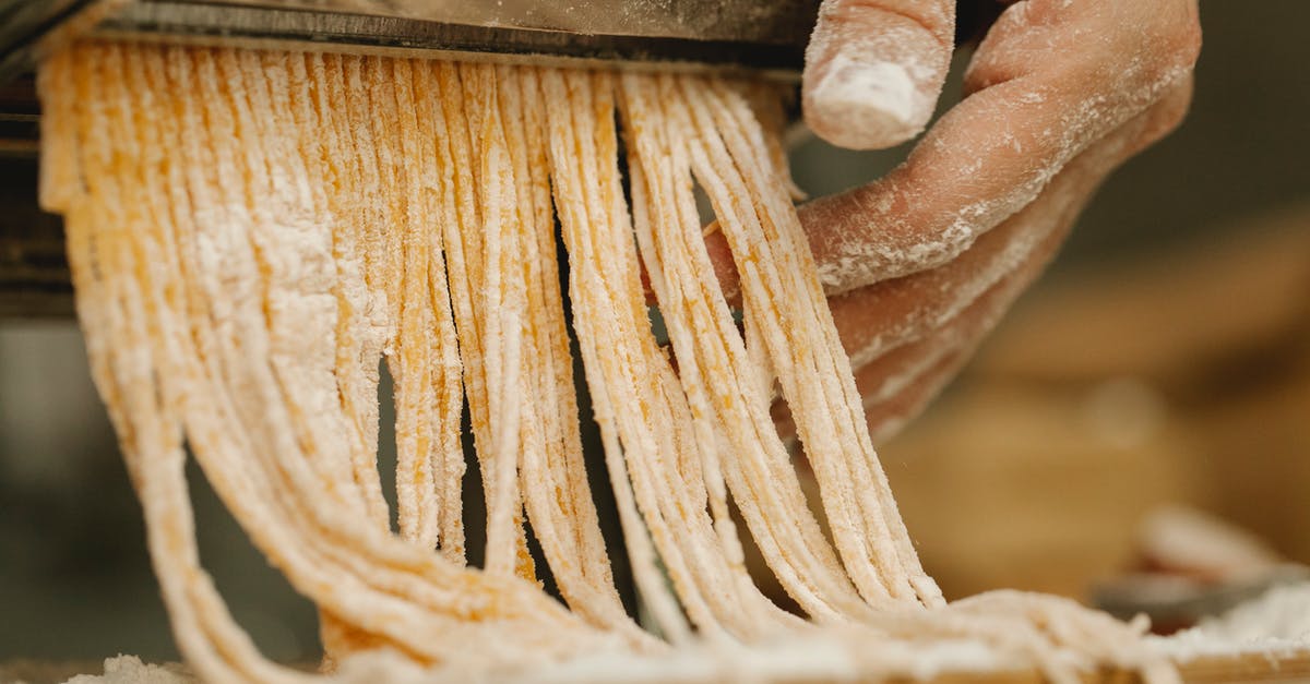 Hand made pasta with wholemeal flour - Crop unrecognizable chef preparing spaghetti from uncooked dough with flour using pasta rolling machine in kitchen