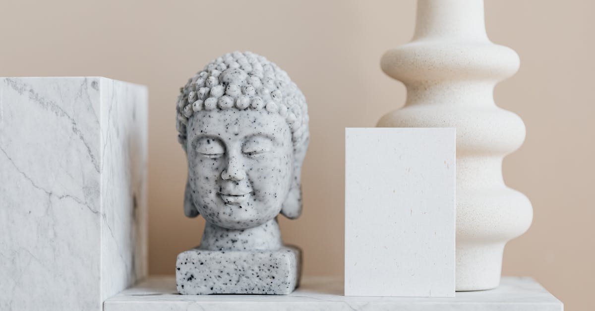 Head space in Weck jars - Granite bust of Buddha placed near white ceramic vase of creative geometric shape and blank card on white marble shelf against beige wall