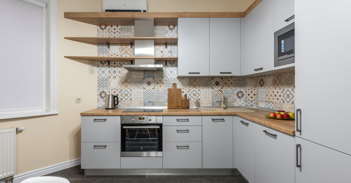 Heating bread in the microwave oven and wetting - Modern kitchen with cabinets and electric stove with oven under hood illuminated by shiny lamp in house