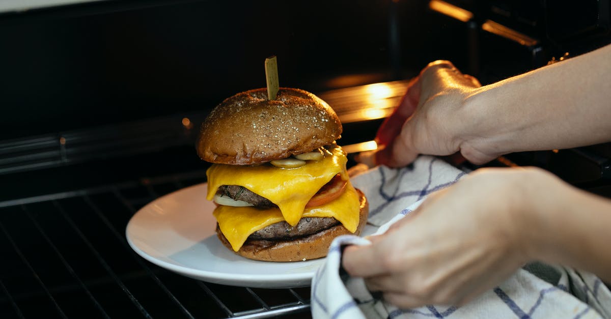 Heating bread in the microwave oven and wetting - From above of unrecognizable person using towel to place burger served on plate in hot oven on rack while cooking