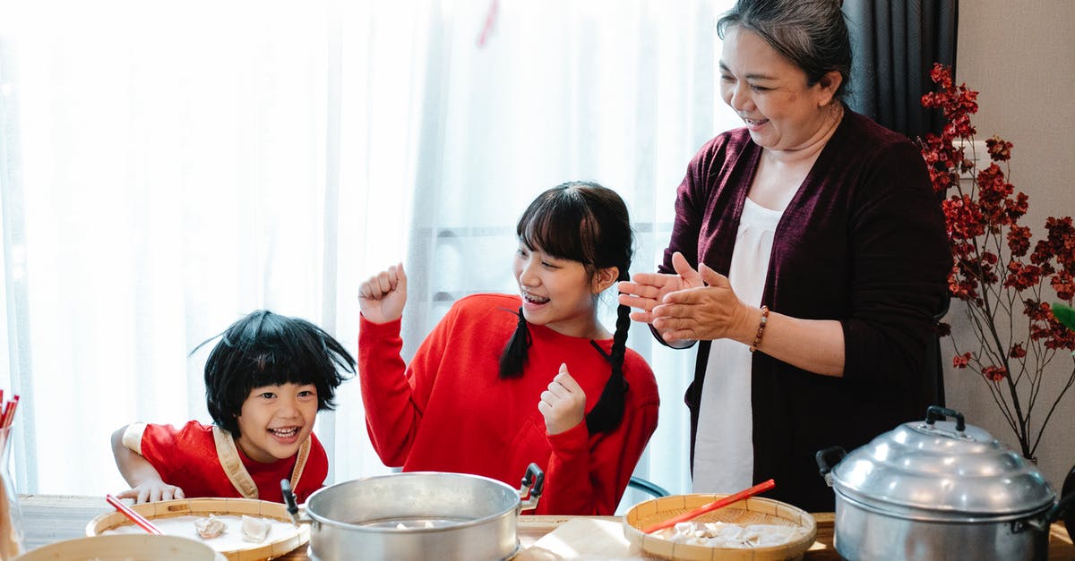 Help buying a copper pan - Cheerful mature Asian woman with teenage granddaughter clapping hands while having fun with little boy helping with jiaozi preparation in kitchen