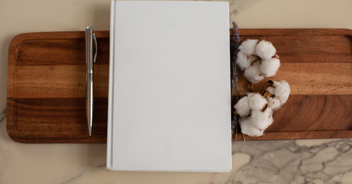 Help finding information on Marble coated woks - Overhead view of composition of empty hardcover book lying between metallic pen and soft cotton flowers on wooden tray with recesses