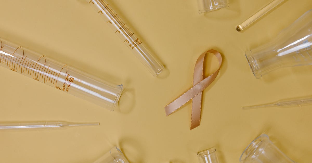 Help freezing chicken breasts - Top view of pink ribbon representing cancer placed on yellow background among glass test tubes and flasks in light studio