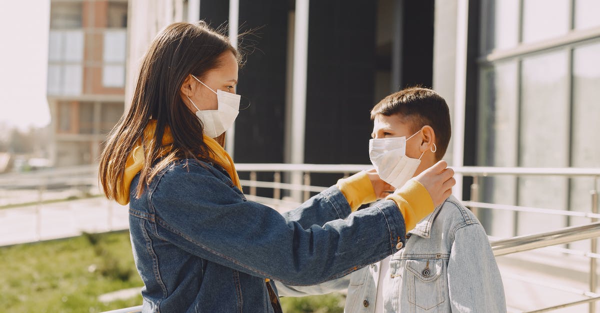 Help me fix my flatbread - Side view of children in casual outfit and protective masks standing in front of each other while girl fixing protective mask on boy face