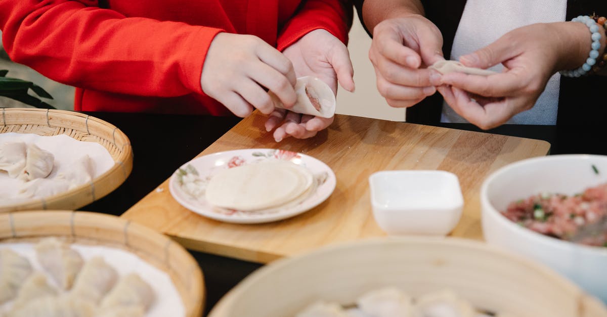 Help wanted to identify this food item (oriental) - Crop anonymous teen girl making traditional Chinese jiaozi dumplings while cooking lunch together at table with ingredients and bamboo steamer