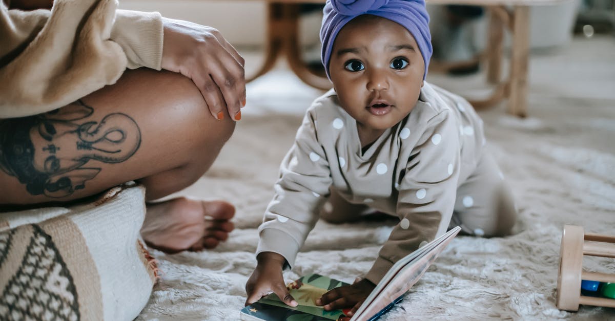 Holes inside a sweet potato - Cute African American toddler on rug with interesting book looking at camera while spending time in room with anonymous black mother