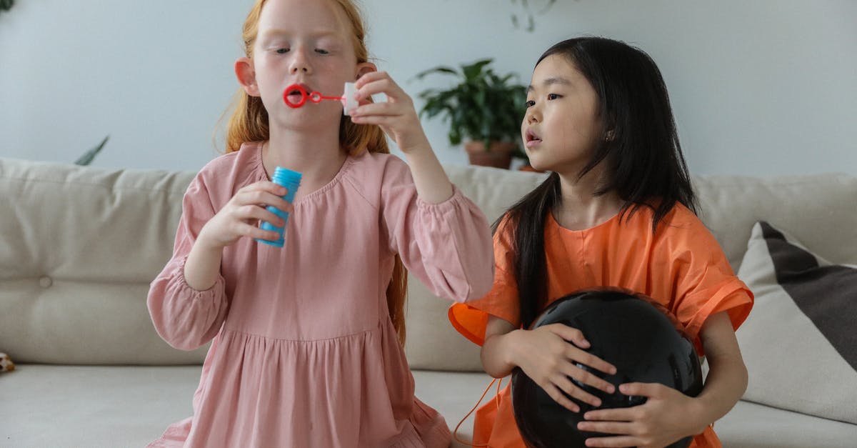 Home made ranch dressing has bubbles. Is it bad? - Adorable little redhead girl in stylish dress blowing soap bubbles while playing with cute Asian girlfriend holding black balloon sitting on sofa at home