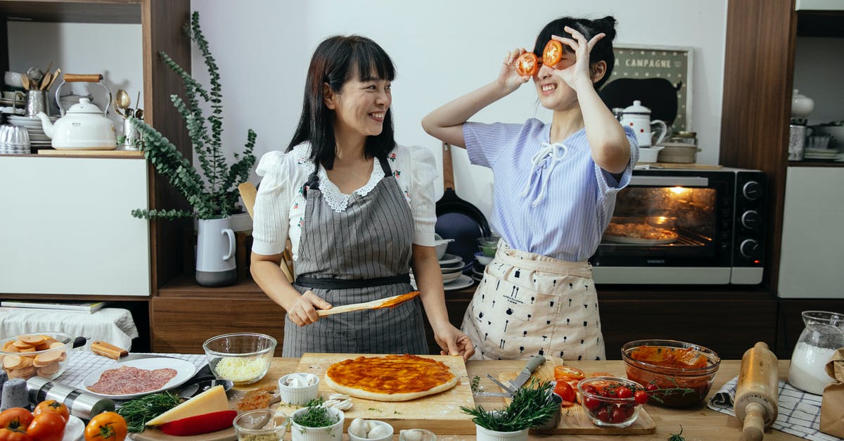 homemade fermented soy sauce safe raw? - Smiling Asian woman spreading tomato sauce on pizza dough while looking at funny female covering eyes with tomato slices in kitchen