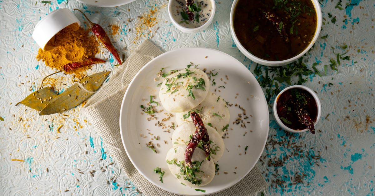 Homemade Pepper Sauce - Suggestion for a serving bottle - Top view of delicious Idli rice cakes with herbs and spicy tomato soup served on table near sauces and scattered spices